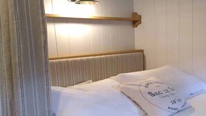 A neatly made bed with white linens and pillows, a wooden headboard, and a wall-mounted light fixture.