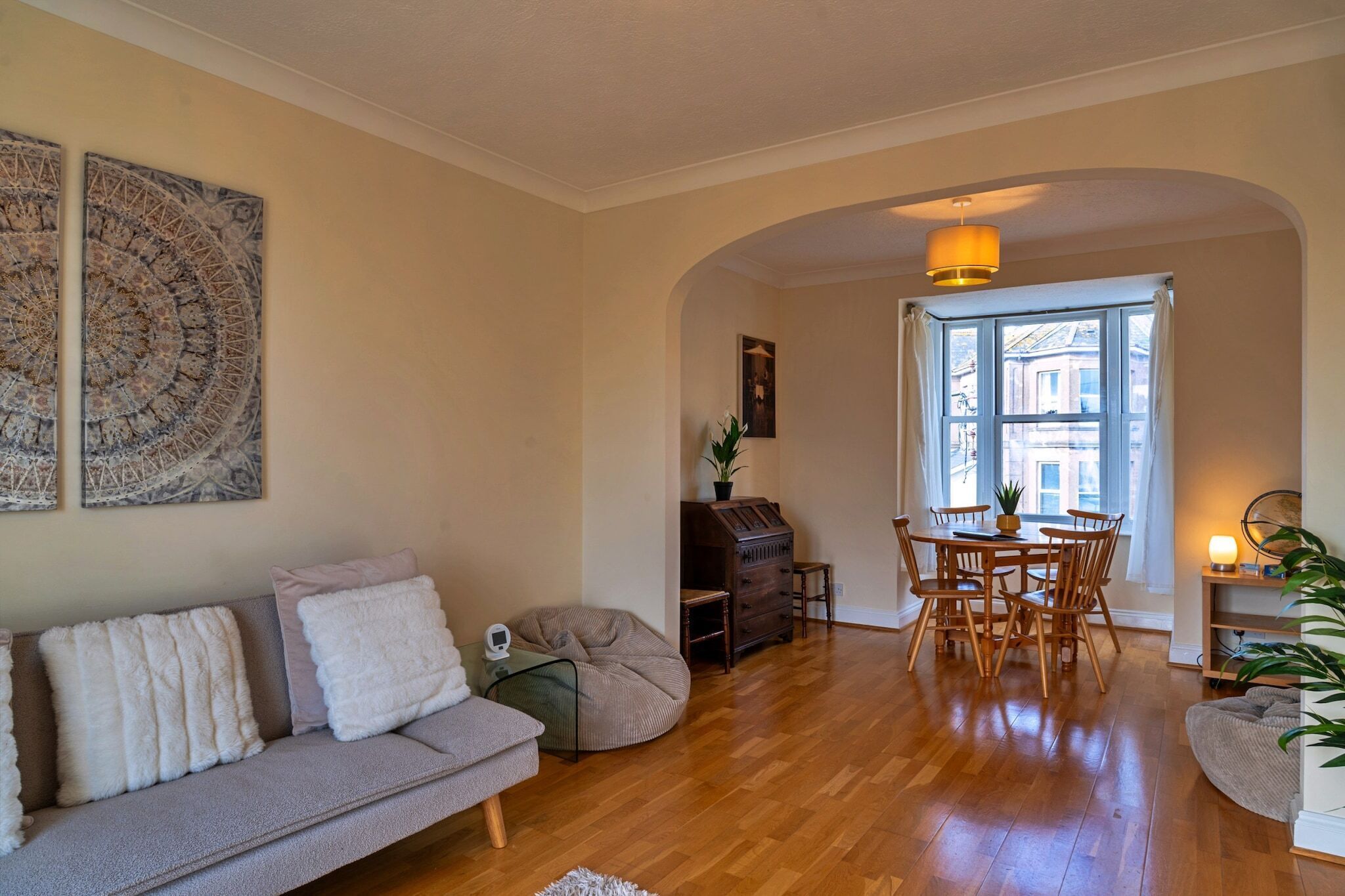 A living room with a sofa, a coffee table, a dining table with chairs, a wooden cabinet, and a large window with curtains.