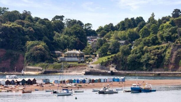 A coastal area with a beach, boats, and a large house overlooking the water.
