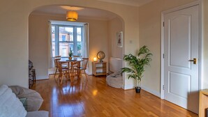A living room with a dining area, wooden flooring, a potted plant, and a white door.