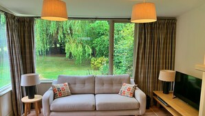 Ein Wohnzimmer mit einer Couch, zwei Lampen, einem Fernseher und einem großen Fenster mit Vorhängen.