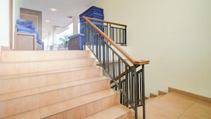 A staircase with a wooden handrail and black balusters, leading to a landing with a blue object on top. - Hotel O Bogor near Taman Safari formerly Ken Raudhah Inn (Cisarua)