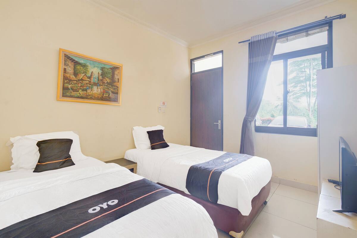 A hotel room with two beds, a painting on the wall, a window with curtains, and a television on a stand.