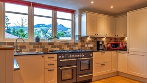 A modern kitchen with a gas stove, oven, and microwave. There are white cabinets and a window with a view of the countryside. - Cottage in Minehead near Exmoor National Park (Minehead)