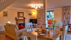 A cozy living room with a sofa, dining table, and chairs. There's a TV, a fireplace, and a window with curtains. - Cottage in Minehead near Exmoor National Park (Minehead)
