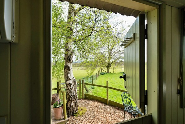 A wooden porch with a bench, a tree, and a view of a grassy field. - Luxurious camping cottage in Nordley, No Deposit (Nordley)