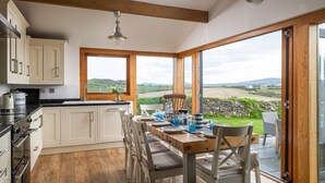 A kitchen with a dining area, wooden flooring, and large windows offering a view of the countryside.