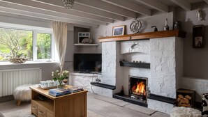 A cozy living room with a fireplace, a television, and a window with a view of greenery.