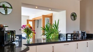 A modern kitchen with white cabinets, a black countertop, and a view into the dining area. - Farmhouse in Weston near Sandy Beaches (Weston-Super-Mare)