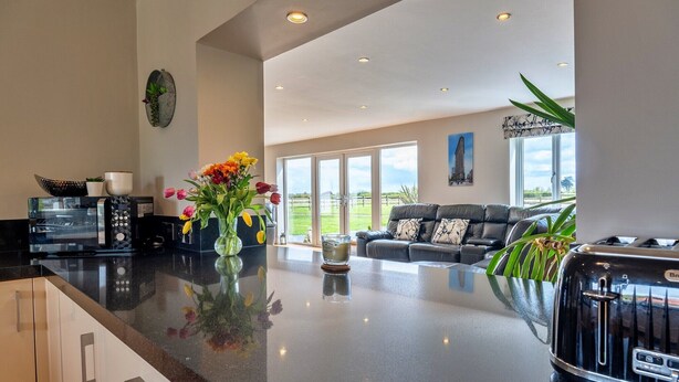 A modern kitchen with a large island, a dining area with a black table and chairs, and a living room with a gray sofa and a painting on the wall. - Farmhouse in Weston near Sandy Beaches (Weston-Super-Mare)