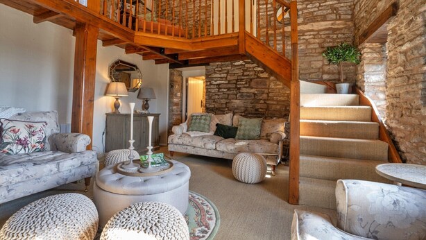 Una sala de estar acogedora con pared de piedra, una escalera de madera y un sofá cómodo.