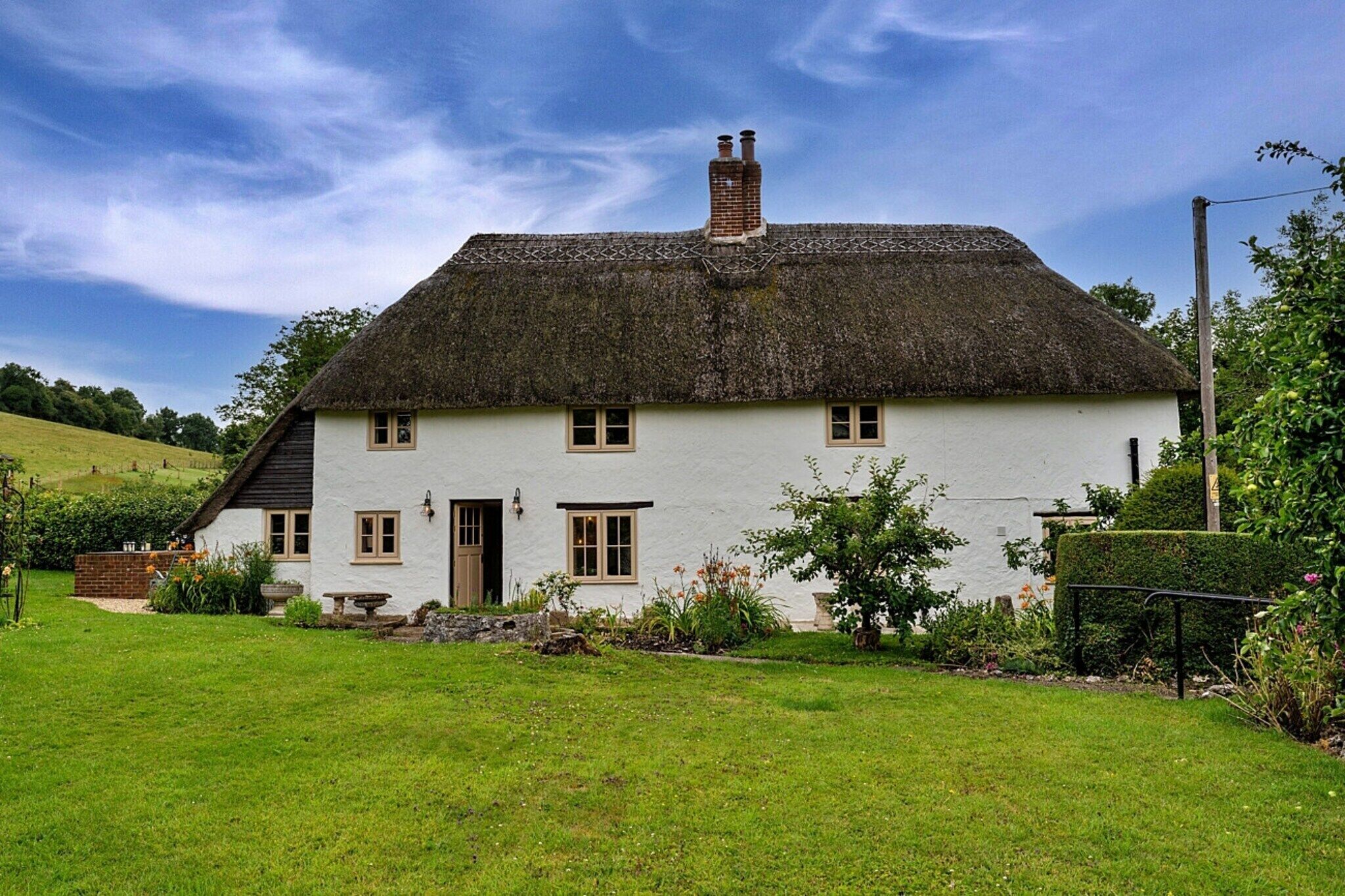 Een wit huis met rieten dak, schoorsteen en een verzorgde tuin.
