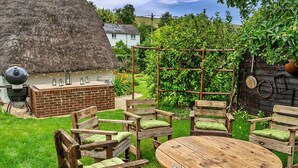 A rustic outdoor seating area with wooden furniture and a thatched-roof barbecue. - Cottage in Dorset near Lulworth Cove (Winterborne Houghton)