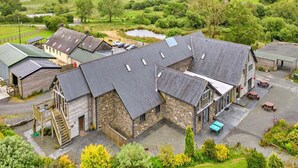 A stone building with a sloped roof, a wooden staircase, and a small outdoor seating area. - Barn in Wales with Swim Spa & Scenic Views (Aberystwyth)