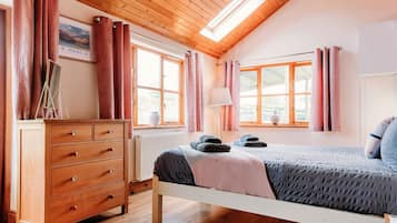 A bedroom with a wooden dresser, a bed with a gray and pink blanket, and a window with pink curtains.