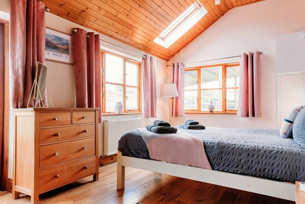 A bedroom with a wooden dresser, a bed with a gray and pink blanket, and a window with pink curtains.