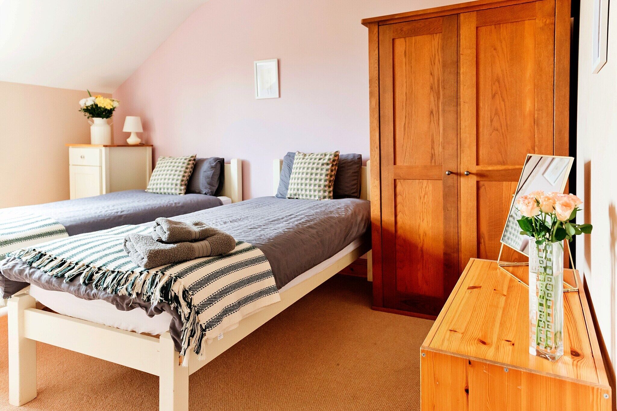 Een slaapkamer met twee bedden, een houten garderobe, een nachtkastje met een vaas en een klein kastje.