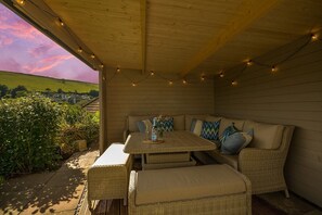 An outdoor patio with wicker furniture, string lights, and a view of the countryside. - Holiday Home in Kingsand near the Beach (Kingsand)
