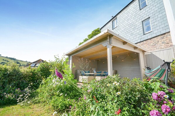 A house with a covered patio area, a hammock, and a garden with various plants and flowers. - Holiday Home in Kingsand near the Beach (Kingsand)