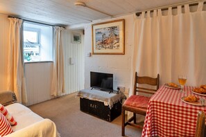 A cozy room with a bed, a television on a chest of drawers, a table with croissants and a glass of drink, and a painting on the wall.