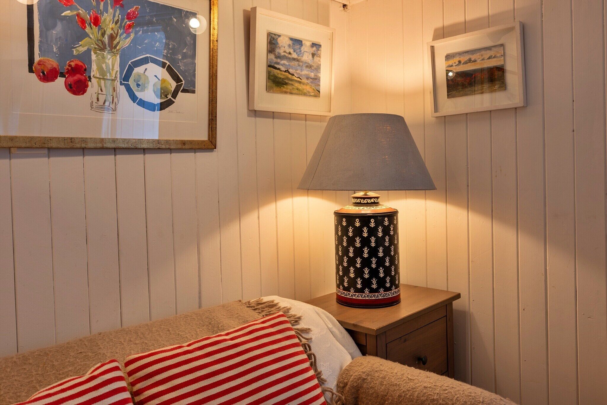 A bedroom with a bed, a nightstand with a lamp, and three framed pictures on the wall.