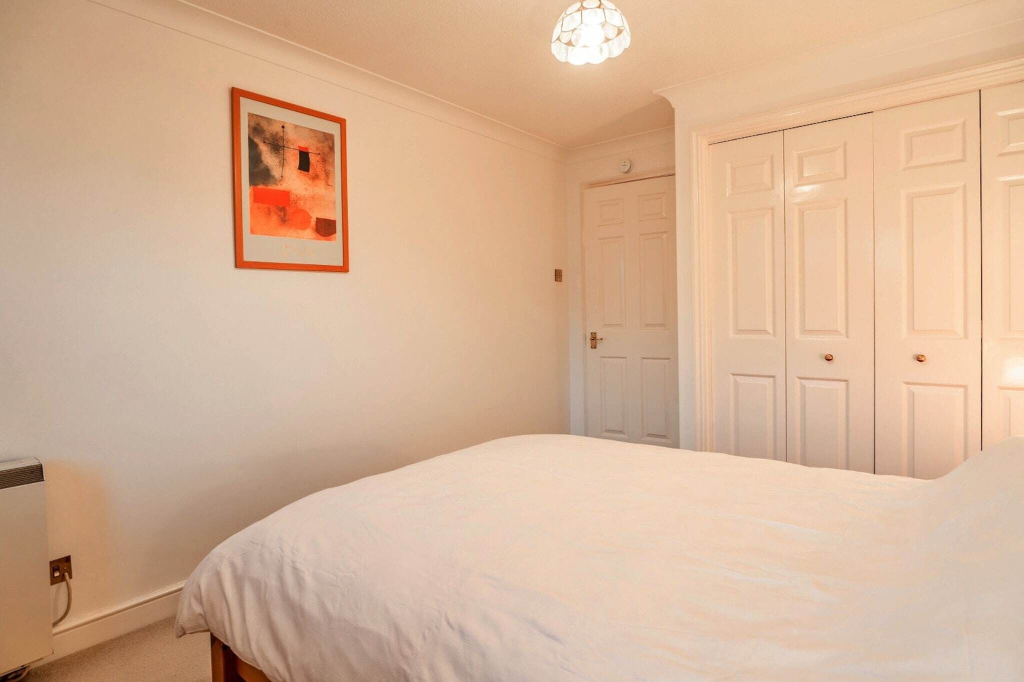 A bedroom with a bed, a white wardrobe, and a framed picture on the wall.