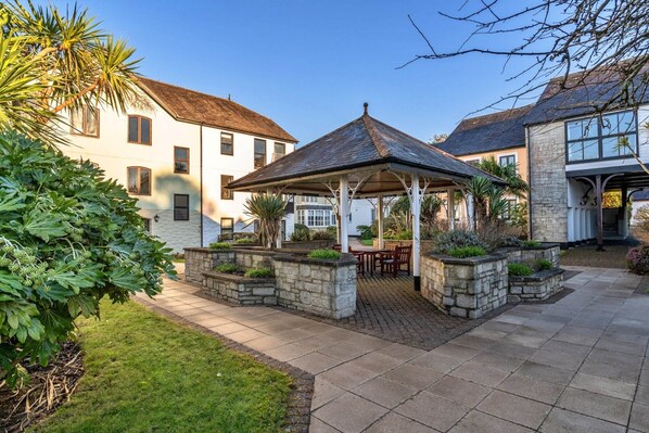 A courtyard with a gazebo, stone planters, and a well-maintained lawn.