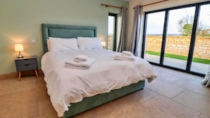 Ein Schlafzimmer mit einem großen Bett, einem Nachttisch und Blick durch eine Glastür.