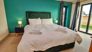 A neatly made bed with white linens and towels, a dark headboard, and two bedside tables with lamps. - Cottage in Cotswolds with Hot Tub & Garden (Little Rissington)