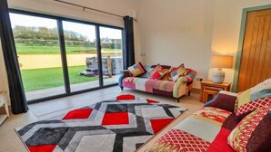 A modern living room with a large window, a sofa set, and a patterned rug. - Cottage in Cotswolds with Hot Tub & Garden (Little Rissington)