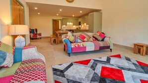A living room with a sofa, a coffee table, and a rug. There is a dining table with chairs in the background. - Cottage in Cotswolds with Hot Tub & Garden (Little Rissington)