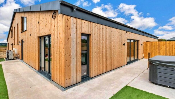A modern wooden building with large glass doors and windows, a concrete patio, and a hot tub. - Cottage in Cotswolds with Hot Tub & Garden (Little Rissington)