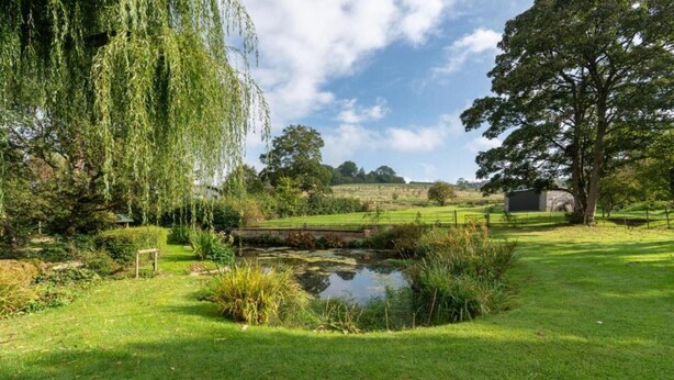 A serene landscape with a pond, lush greenery, and a distant building. - Barn in Cotswolds near Bourton-on-the-Water (Little Rissington)