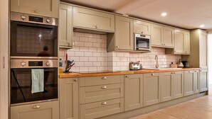 A kitchen with beige cabinets, a double oven, a microwave, and a tiled backsplash. - Barn in Cotswolds near Bourton-on-the-Water (Little Rissington)
