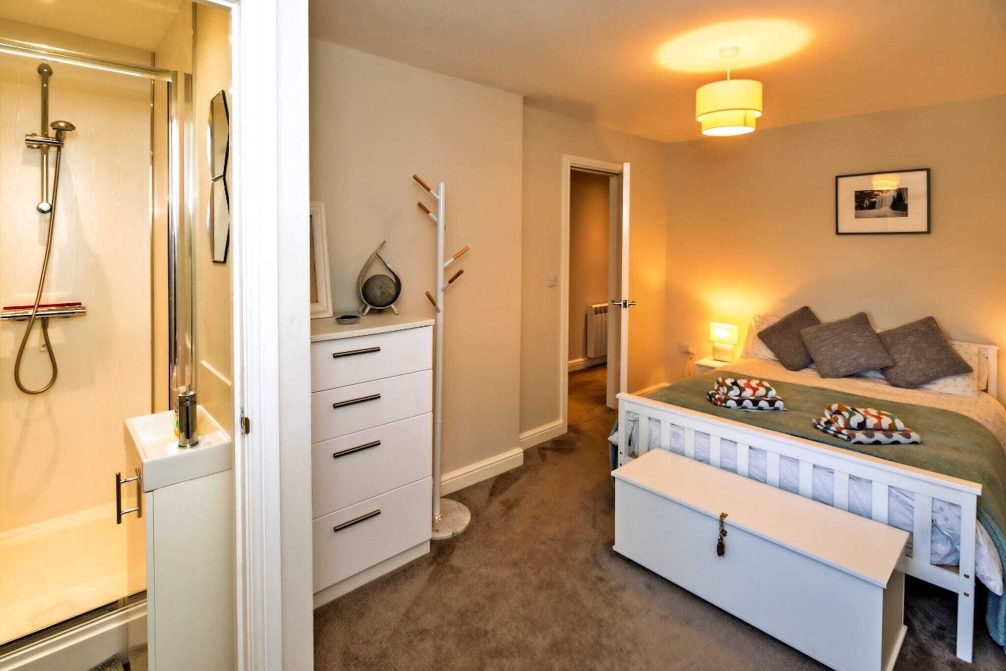 A bedroom with a bed, bedside table, and a nightstand. There is a bathroom with a shower, sink, and toilet.