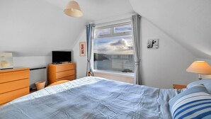 A bedroom with a bed, a dresser, a television, and a window with curtains.