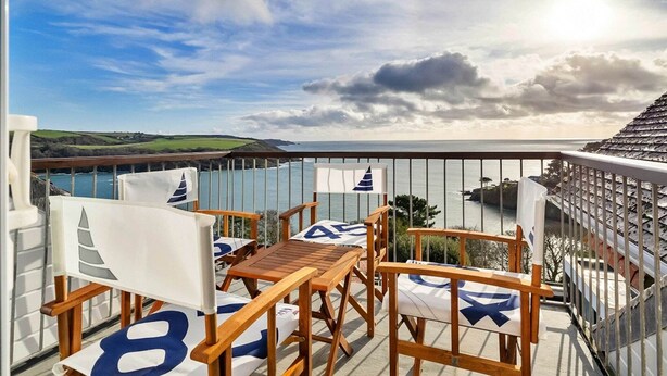 A balcony with wooden furniture and a view of the sea.