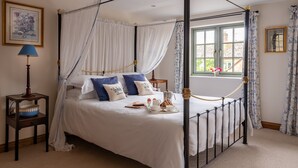 Un lit à baldaquin avec une literie blanche et des coussins bleus, une table de chevet avec une lampe et une fenêtre avec des rideaux.