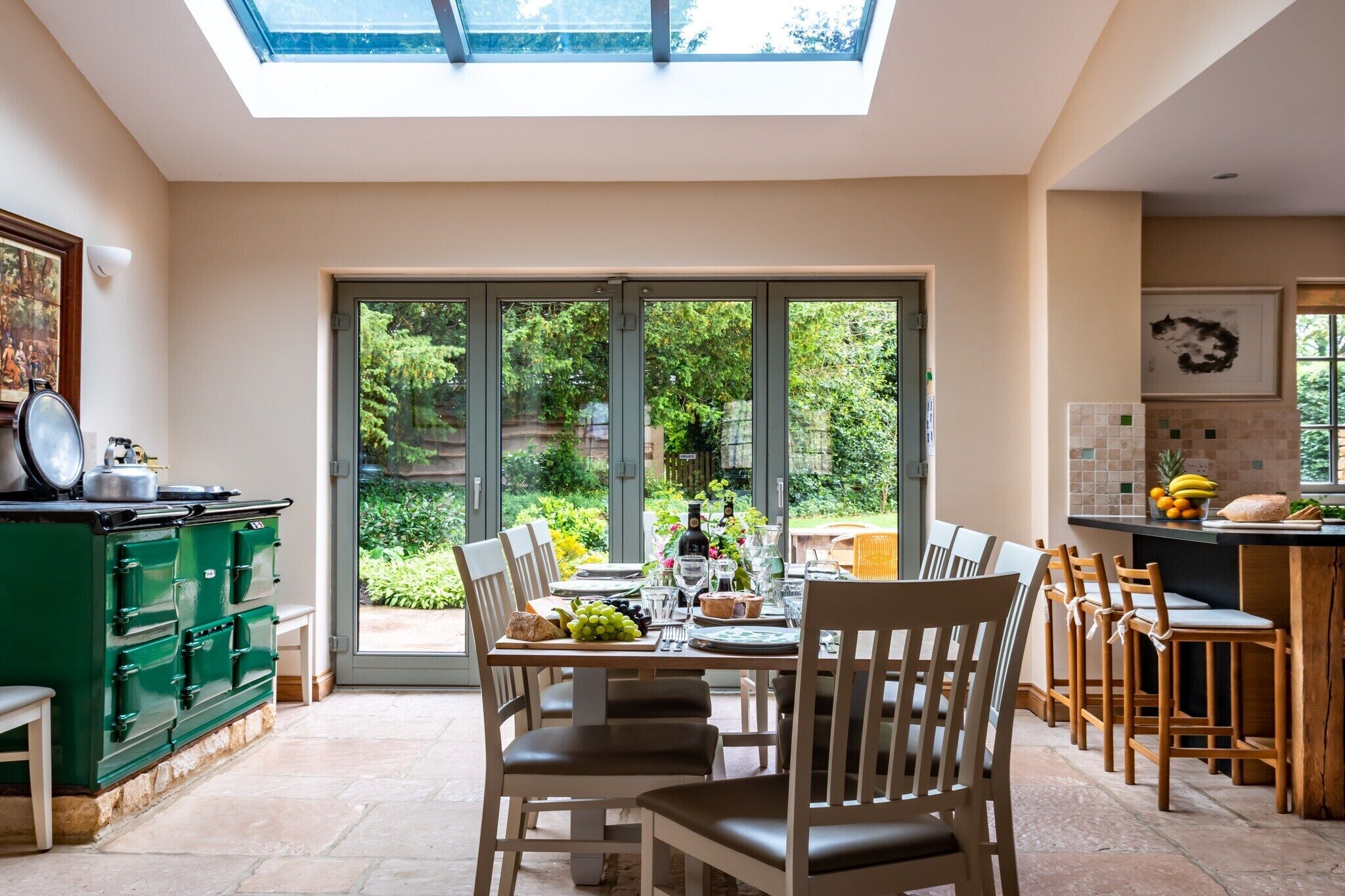 Une cuisine moderne avec un coin repas, de grandes portes-fenêtres coulissantes donnant sur un jardin et une commode verte.