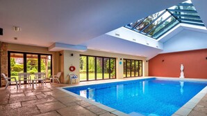 Une piscine intérieure dotée d’une verrière, d’un sol en pierre et offrant une vue sur l’extérieur.