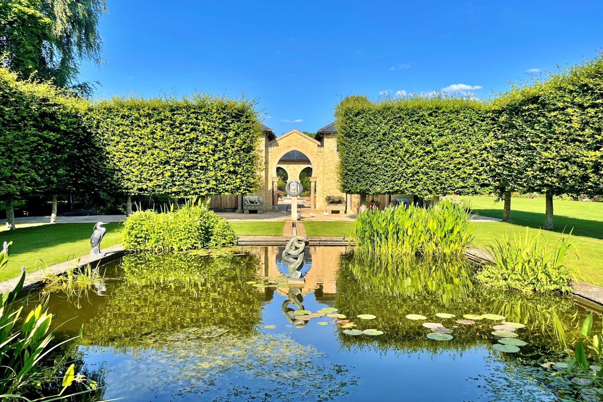 A serene garden with a central fountain, surrounded by neatly trimmed hedges and a calm pond with lily pads.