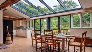 A spacious dining area with a large table and chairs, a kitchen in the background, and a skylight above. - Villa in Pollença with Sea Views & Pool (Kingham)