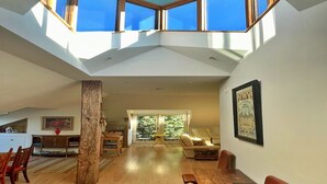 A spacious living area with a high ceiling, skylights, a wooden dining table, and a sofa. - Loft in Cotswolds with Pool & Scenic Gardens (Kingham)
