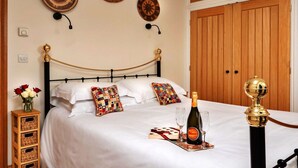 A neatly made bed with a bottle of champagne and a glass, a decorative wall hanging, and a wooden door in the background. - Loft in Cotswolds with Pool & Scenic Gardens (Kingham)