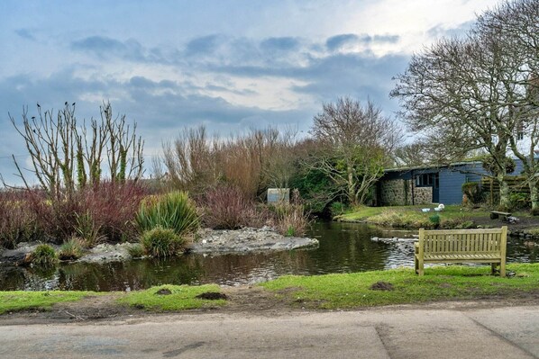 A serene riverside setting with a bench, a small building, and a bridge.
