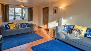 A living room with two sofas, a blue rug, a wooden door, and a window with curtains. - Holiday Home near Nanjizal Cove & Coastal Path (Sennen)