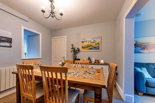 A dining area with a wooden table and chairs, a chandelier, a painting, and a view of a snowy landscape through an open door.