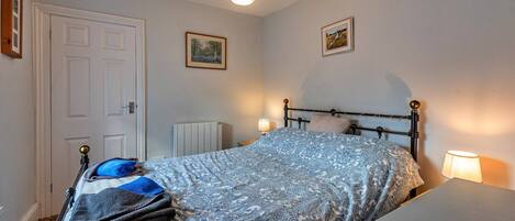 A bedroom with a bed, bedside tables, a radiator, and two framed pictures on the wall.