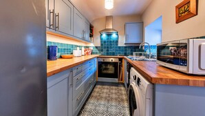 Cocina compacta con armarios grises, horno integrado, microondas y lavadora.