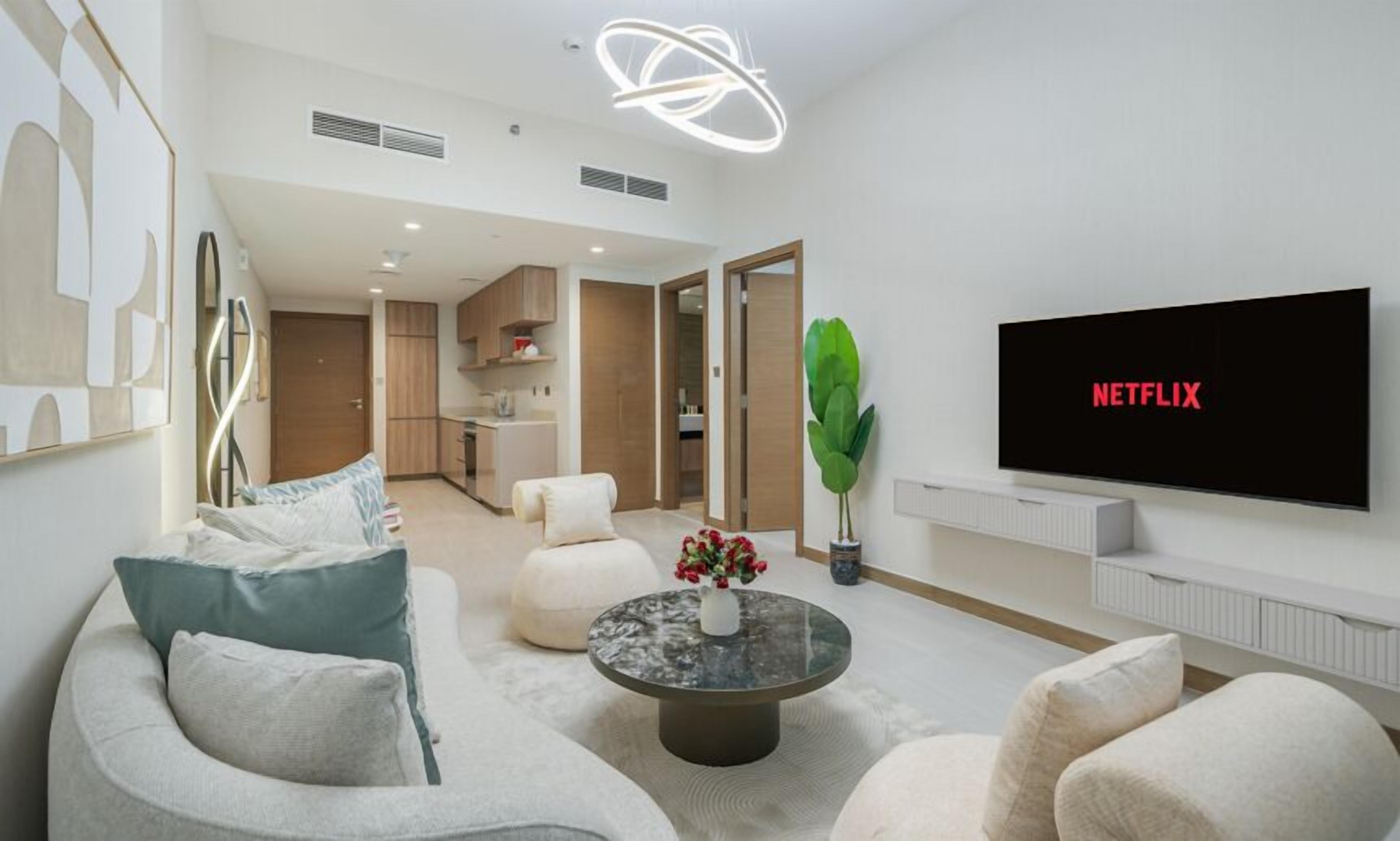 Uma sala de estar moderna com uma televisão de tela plana exibindo o logotipo da Netflix, uma mesa de centro redonda com um vaso de flores e um sofá com almofadas.